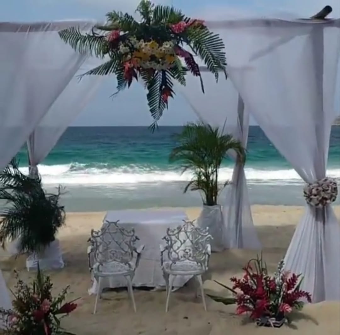 Arco de boda con velos blancos y flores frente al mar